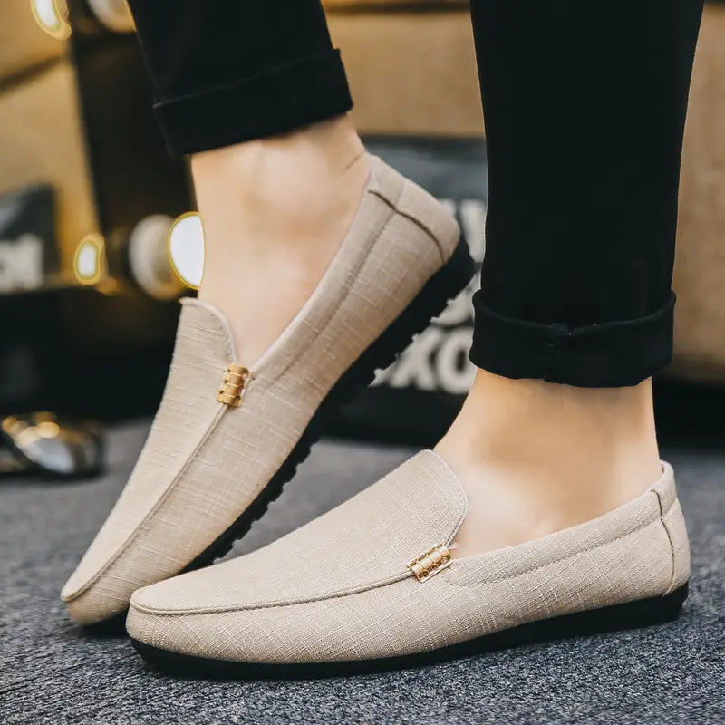 Mocassins à enfiler pour homme en toile à texture lin de couleur beige, avec détail de boucle métallique ton or sur l’empeigne.