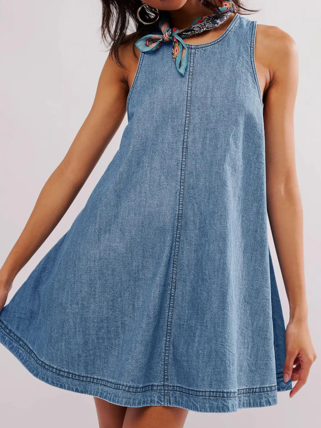 Ein ärmelloses, hinten offenes Schleifen-Detail aus Denim-Minikleid in mittlerer Blau-Waschung mit rundem Halsausschnitt, wobei ein gemustertes Tuch zu einer Schleife gebunden ist, ergänzt durch ein hinten offenes Schleifen-Detail.