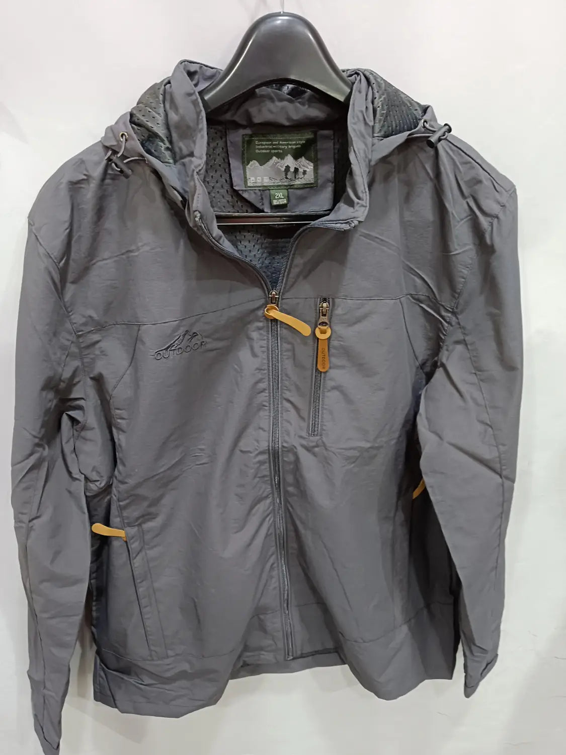 Chaqueta de senderismo con capucha impermeable color gris, con tiradores de cremallera amarillos y un logotipo bordado sutil en el pecho.