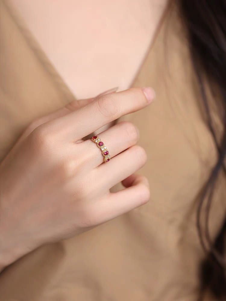 An 18k gold plated band ring featuring alternating pigeon blood ruby and clear diamond stones in a delicate design.