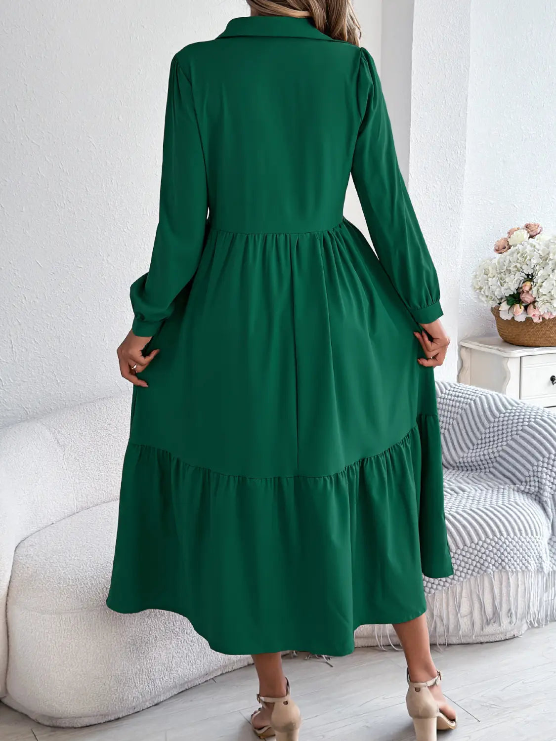 A woman wears a long sleeve emerald green tiered button down midi dress with a collared neckline and gathered waist.