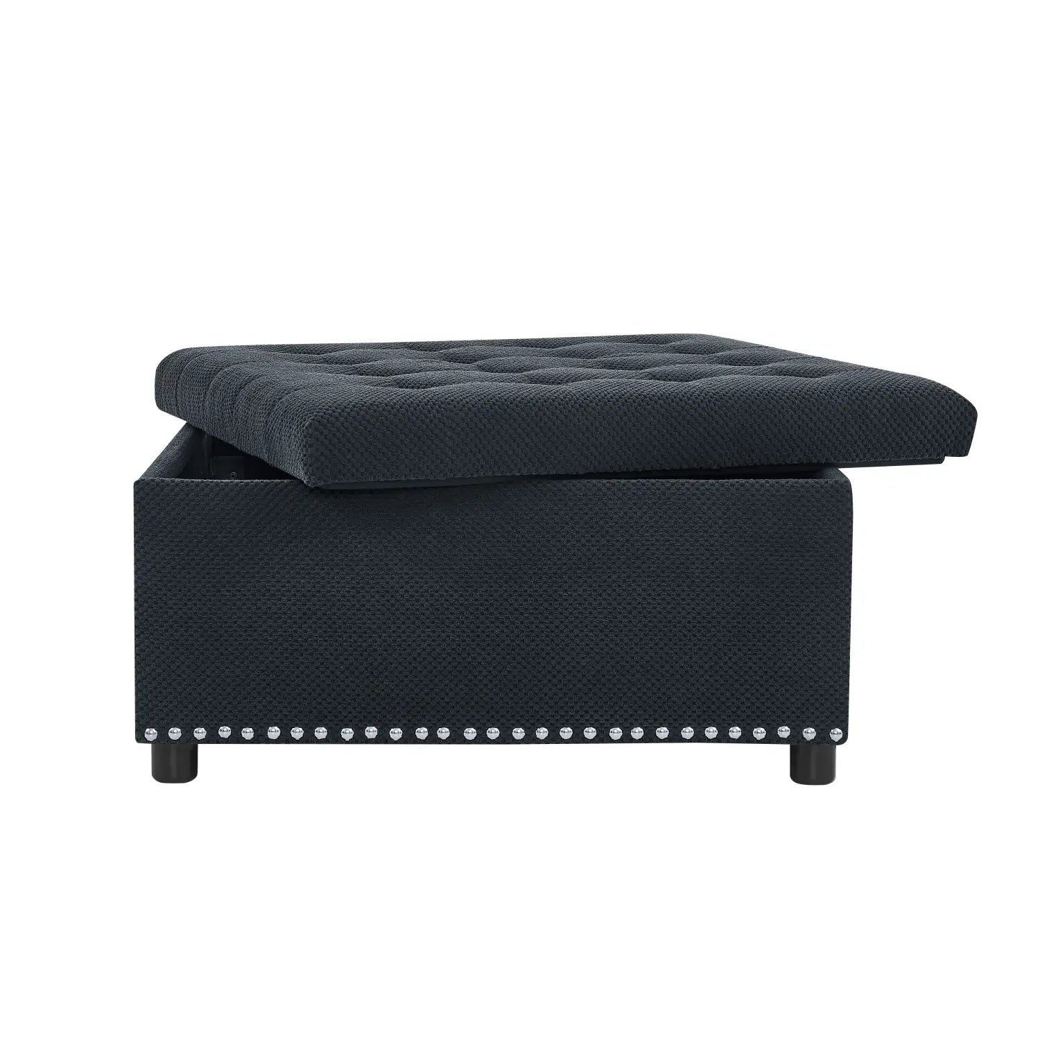 Black tufted storage ottoman with textured fabric finish and decorative silver nailhead trim along the base.