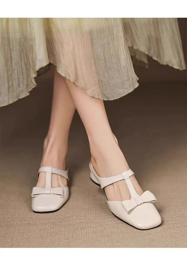 Cream-colored leather bow closed toe square-toe flats for women featuring a t-strap and decorative bow on the front.