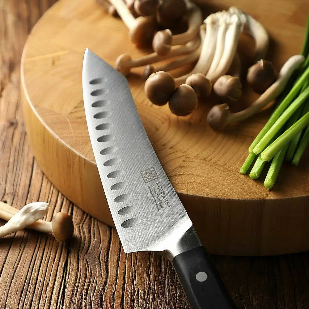 Couteau de chef élégant en acier inoxydable, doté d’un manche noir, avec des trous ovales distinctifs le long de la lame, inclus dans un ensemble de couteaux de chef comprenant des ciseaux de cuisine en acier inoxydable.