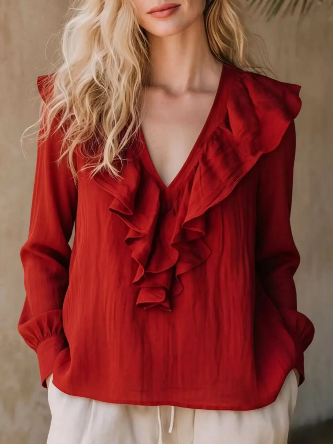Une blouse en lin rouge vif à encolure en V et manches longues, avec des détails de volants qui s’écoulent le long de l’encolure et des manches, réalisée dans un tissu léger légèrement texturé.
