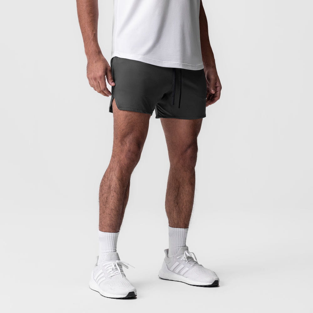 Men quick dry athletic sports shorts in dark gray featuring a drawstring waist and side pockets worn by a model with a white tank top and matching sneakers.