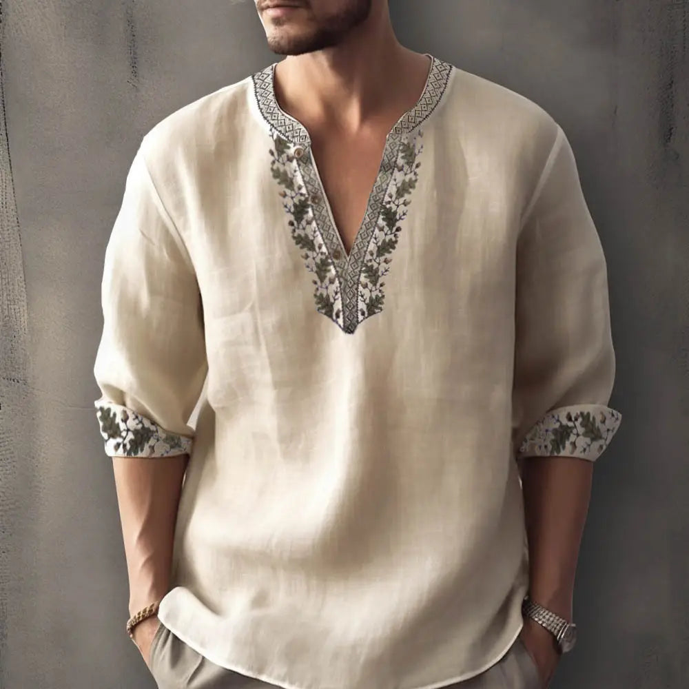 Beiges Leinenhemd mit floraler Musterung, V-Ausschnitt und aufwendigen dunkelgrünen sowie schwarzen bestickten floralen Motiven am Ausschnitt und an den umgeschlagenen Bündchen, ideal für das Tragen als Sommerpullover.