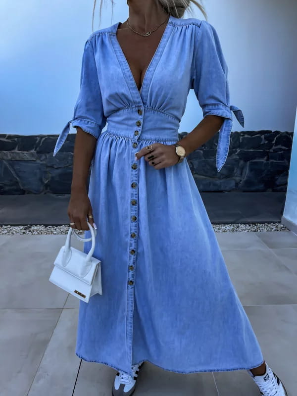 A light blue denim midi dress with puff sleeves, v-neck, button-front closure, and tied cuffs.