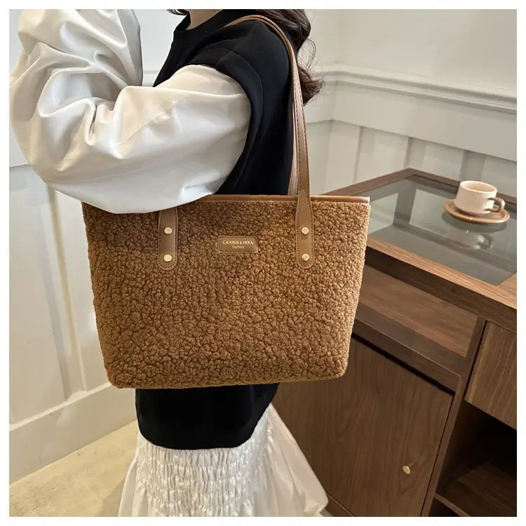 A tan plush teddy bear-style brown faux fur tote bag with brown leather handles and a small metallic brand plaque.