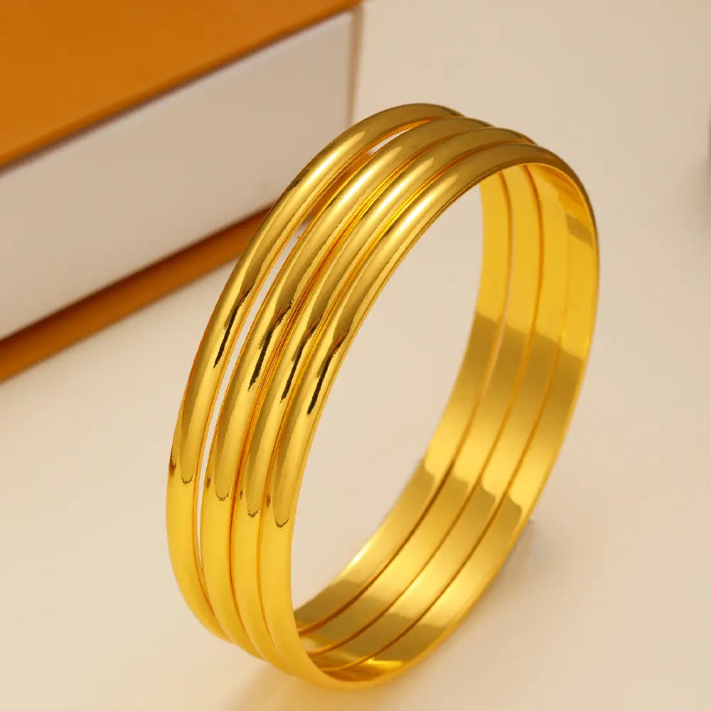 Set of four sleek 18k gold plated minimalist stackable bangles with a polished smooth reflective finish.