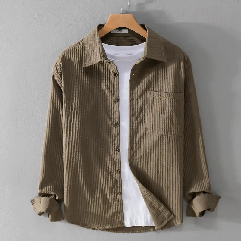 Chemise homme décontractée à manches longues en velours côtelé beige, avec un col classique et une poche poitrine, présentée sur un cintre en bois.