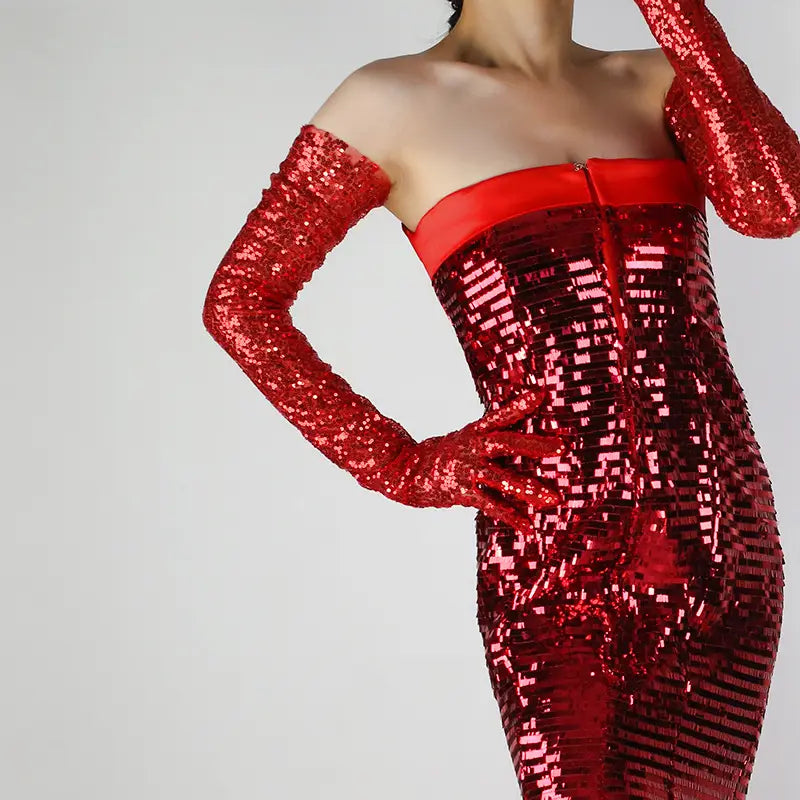 A dazzling red sequined off-the-shoulder dress with long matching mesh finger gloves featuring a sleek satin bandeau top and a fitted silhouette.