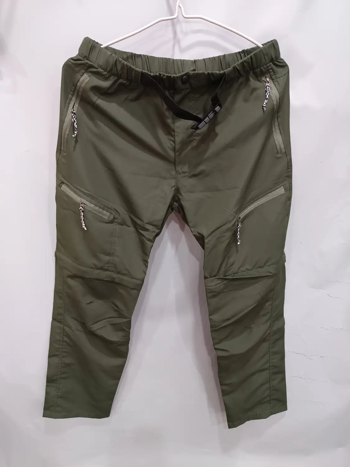 Olive green convertible tactical hiking pants featuring multiple zippered pockets and an elastic waistband designed for outdoor use.
