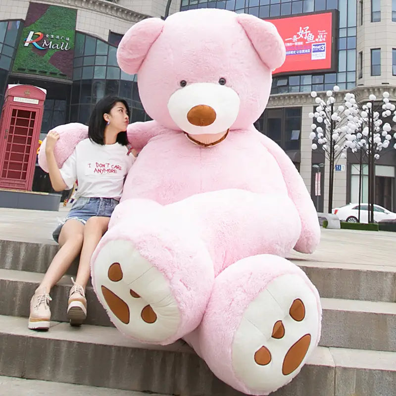 Ein flauschiger pinkfarbener Teddybär mit weißen Pfoten und brauner Nase, der auf Stufen sitzt, ist ein großer weicher Stofftier-Artikel, erhältlich in den Größen 1 Meter und 3,4 Meter.