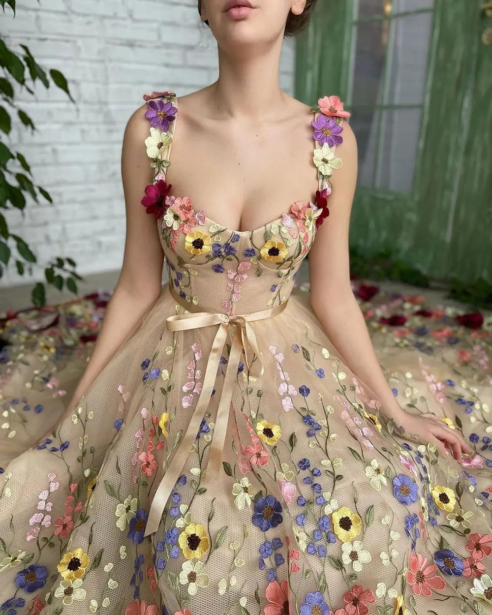 A delicate beige tulle prom gown featuring exquisite 3d multi-colored floral embroidered appliqués and a matching satin ribbon belt.