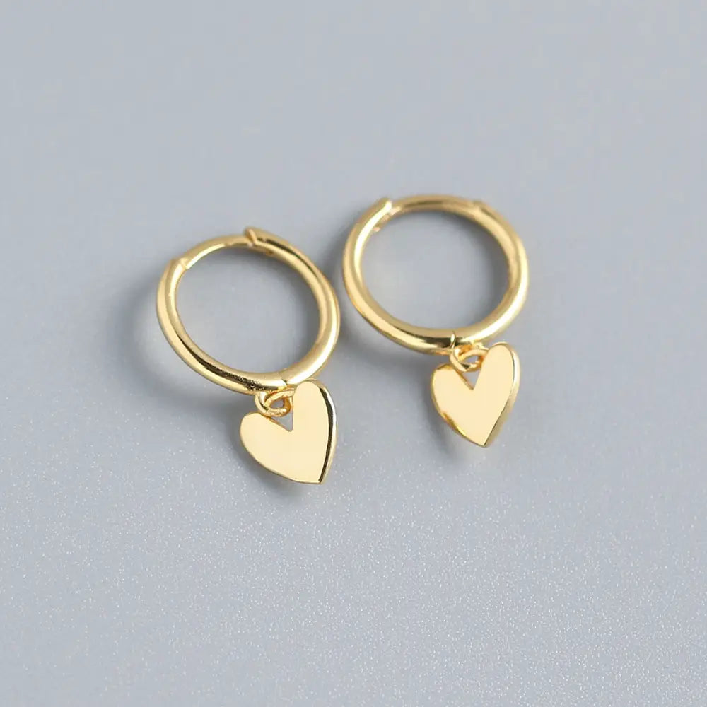 Minimalistische goldfarbene herzförmige Anhänger-Creolen mit polierter Metalloberfläche.