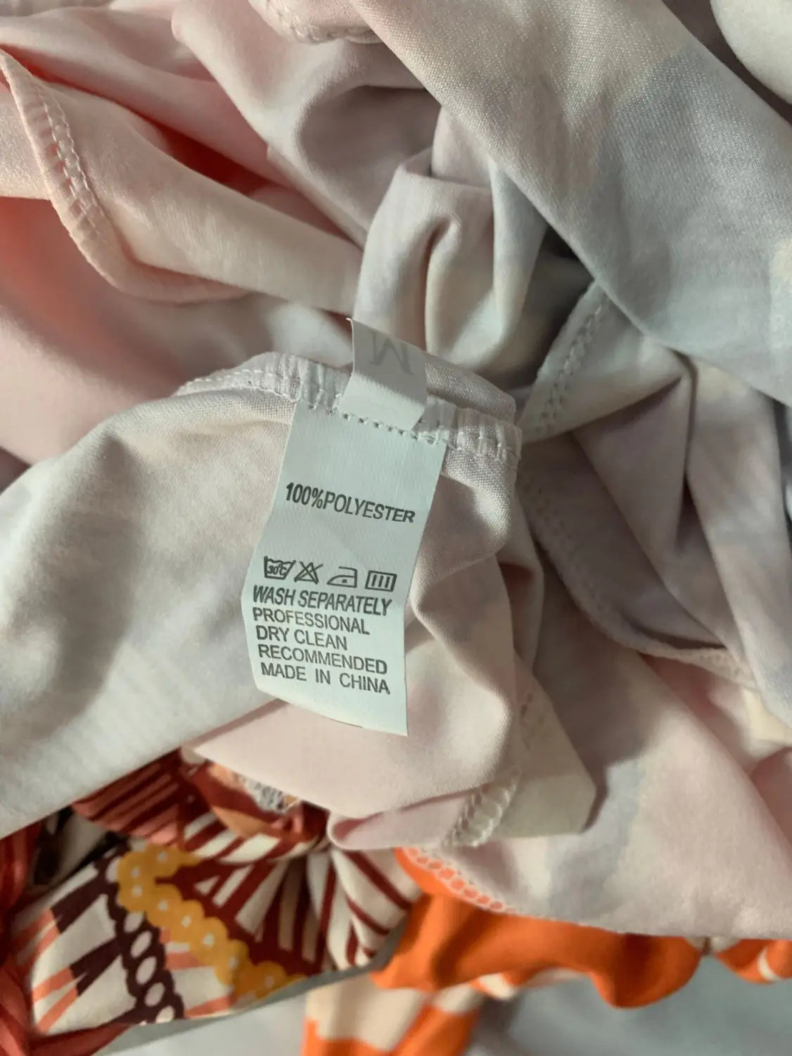 A white polyester garment care label with black text showing 100 percent polyester composition on the back side of a printed v-neck geometric wrap midi dress.