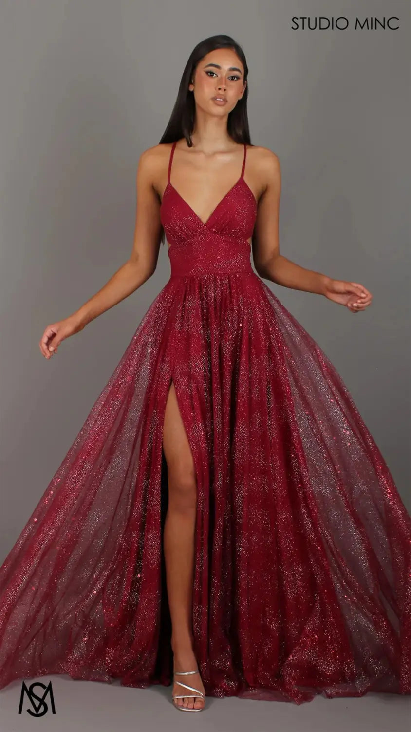 A shimmering burgundy sequined ball gown with a deep v-neckline, delicate spaghetti straps, and a high slit designed as a maxi evening gown.