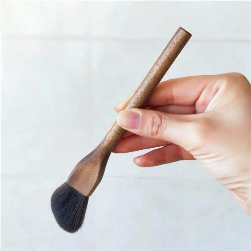 A sleek, dark brown walnut wood handled makeup brush with dense black soft fiber bristles.