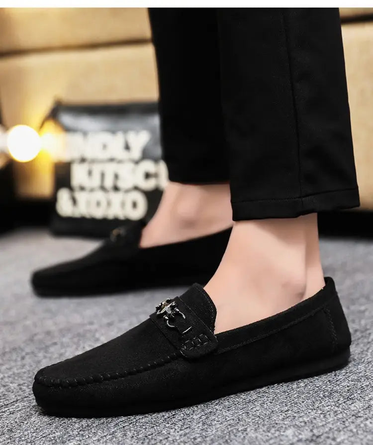 Mocassins à enfiler en daim noir pour homme, comportant un détail de boucle métallique en mors de cheval et un design à enfiler.