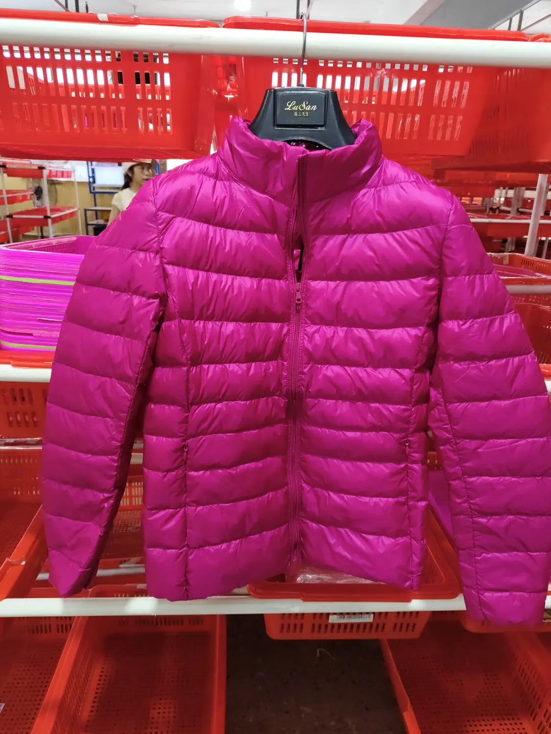 Eine kräftige Fuchsiafarbene Slim-Down-Steppjacke mit Steppdesign und Stehkragen, die auf einem schwarzen Bügel präsentiert wird.