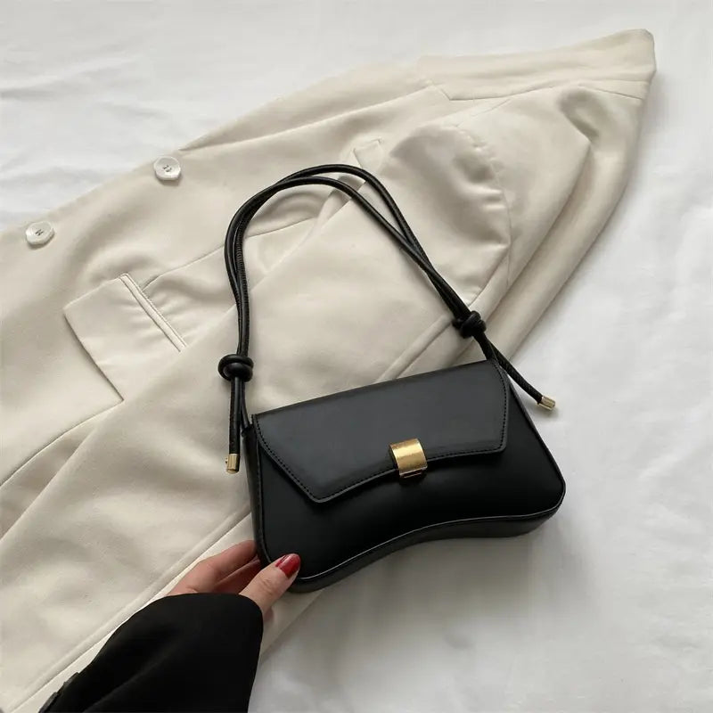 Minimalist faux leather structured shoulder bag in black featuring a gold-tone rectangular clasp and an adjustable black crossbody strap.