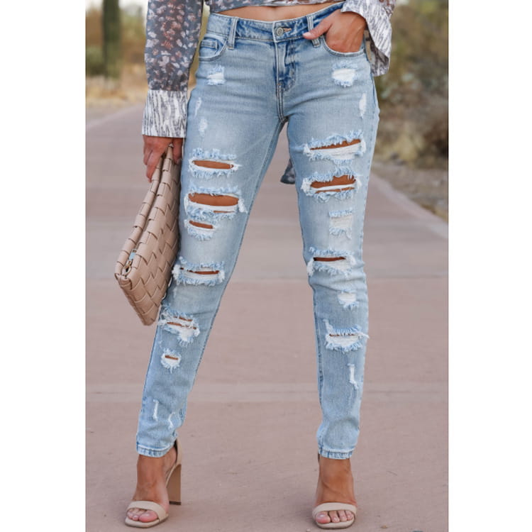 Los pantalones vaqueros ajustados tipo skinny de mezclilla con efecto lavado claro y con roturas presentan múltiples cortes desgastados y bordes deshilachados en un estilo casual.