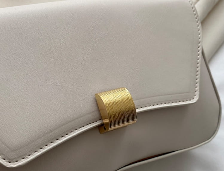 Cream-colored minimalist faux leather structured shoulder bag with a textured gold-tone rectangular clasp.