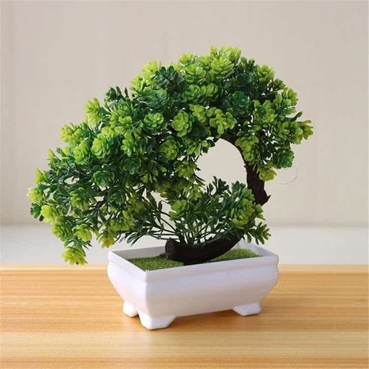 Ein kompaktes künstliches Bonsai-Bäumchen mit üppigem grünem Laub und einem dunkelbraunen Stamm in einem weißen Keramiktopf, der für eine stilvolle Wohn- oder Büroeinrichtung ausgelegt ist