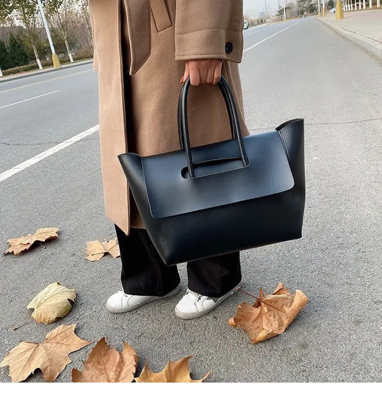 Black leather vintage structured tote bag with top handles and a minimalist flap closure.