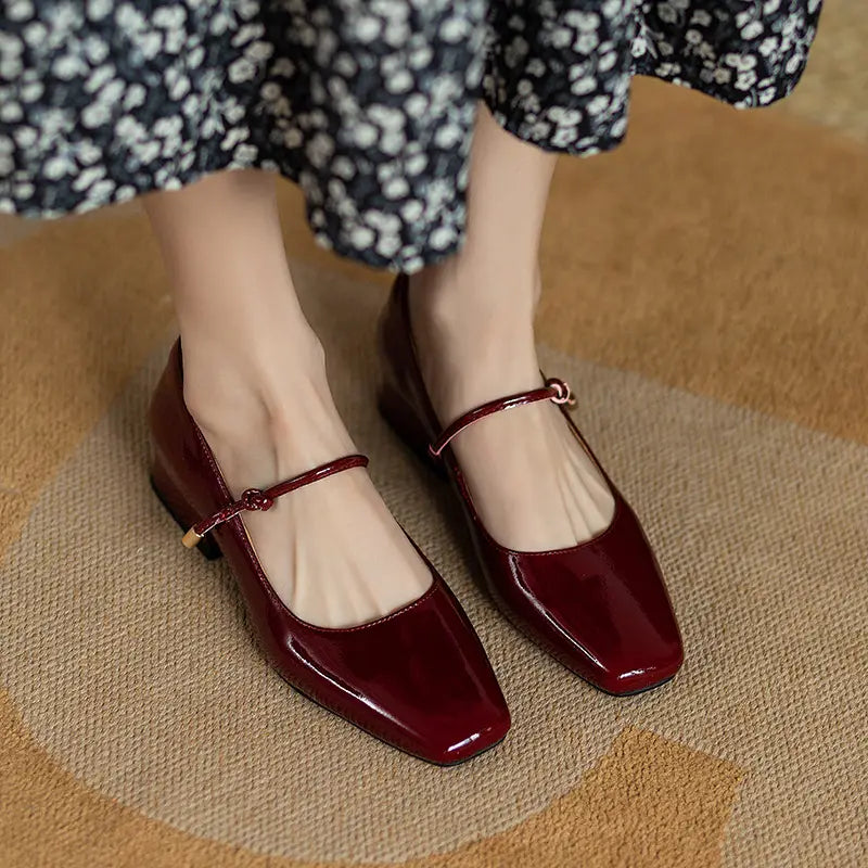 Burgundy patent leather square toe mary jane flats with a low block heel and gold tone buckle strap.