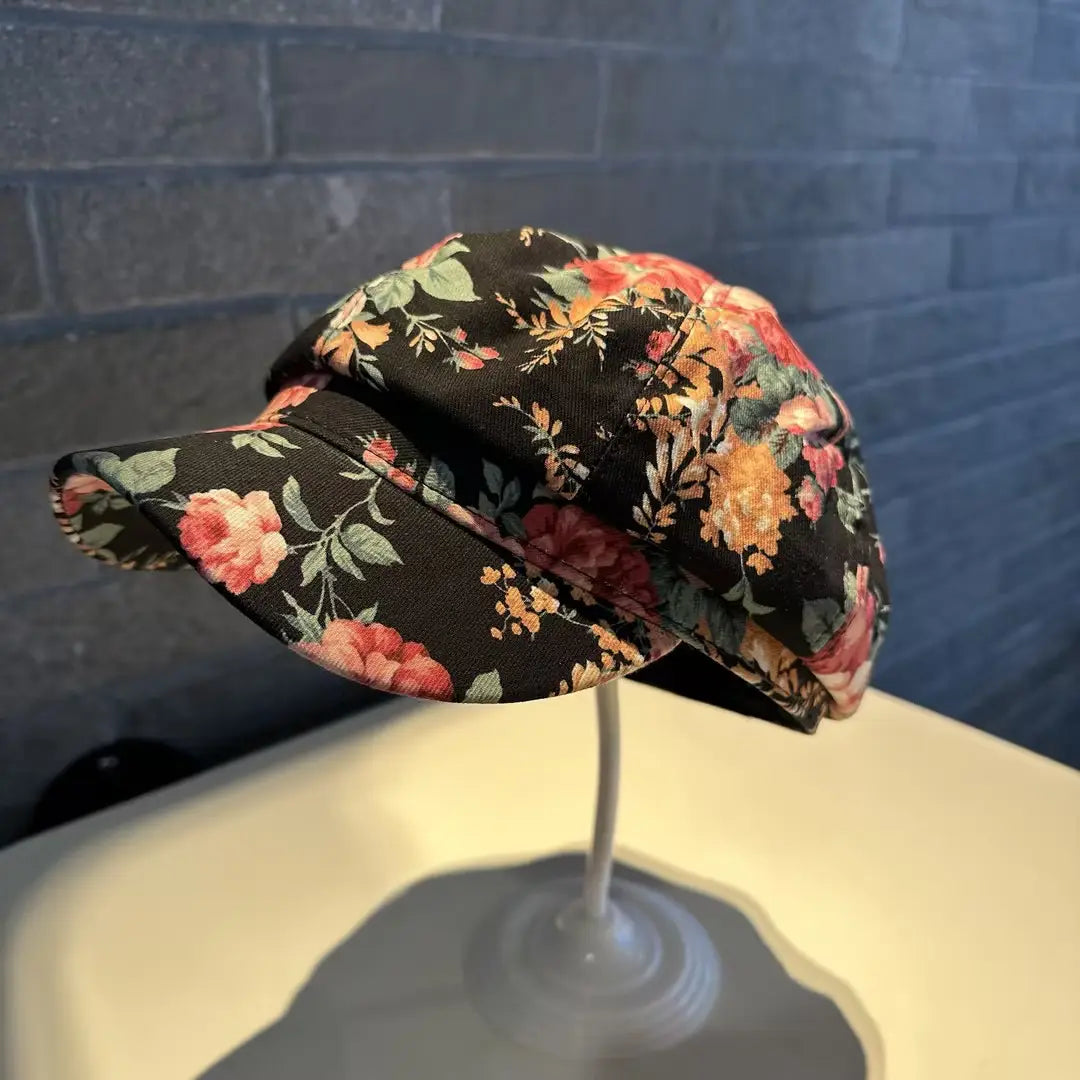 A black fabric floral newsboy cap for women featuring pink orange and green blossoms in a black and white pattern.