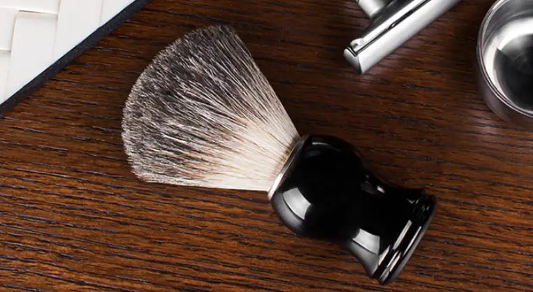 Badger hair shaving brush with black ceramic handle and dense tapered head of white and gray badger bristles.