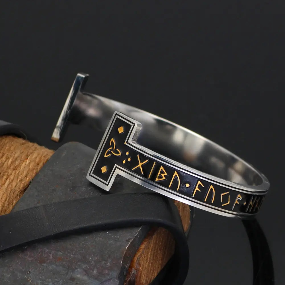 Adjustable viking rune titanium steel open cuff bracelet with a silver finish black inlay gold colored norse runes and an ornate cross design.