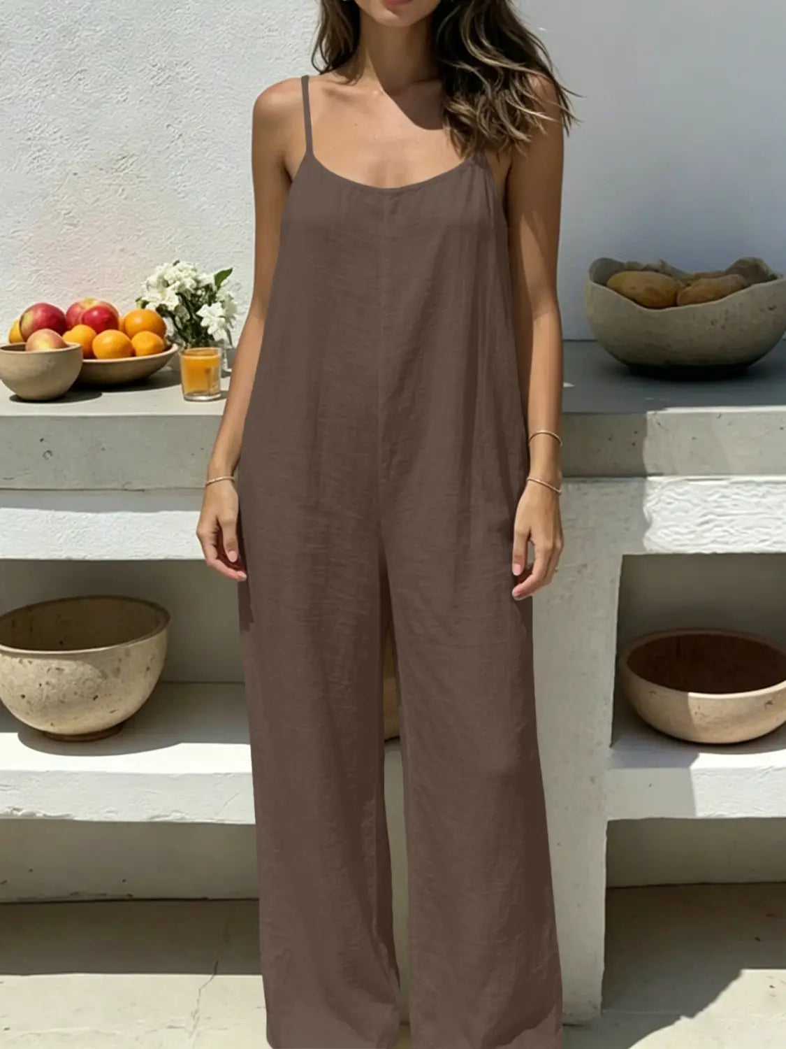 A flowing taupe linen wide leg backless jumpsuit with thin spaghetti straps.