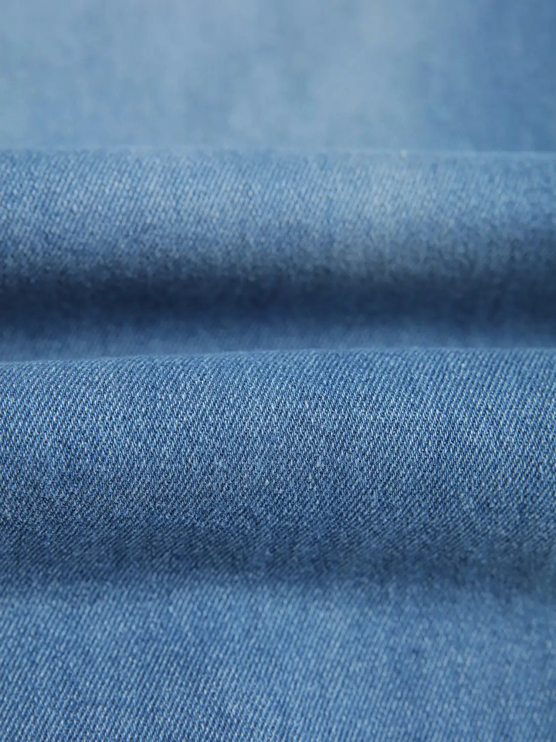 Blue denim fabric with a textured woven pattern used in men’s distressed slim fit stretch denim jeans.