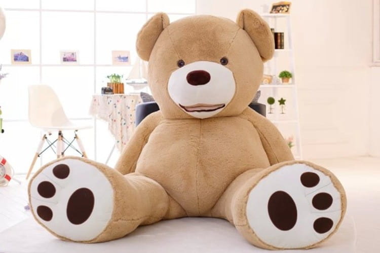 A plush tan giant teddy bear plush toy with white paws and a brown nose featuring an unfilled leather shell sitting upright.