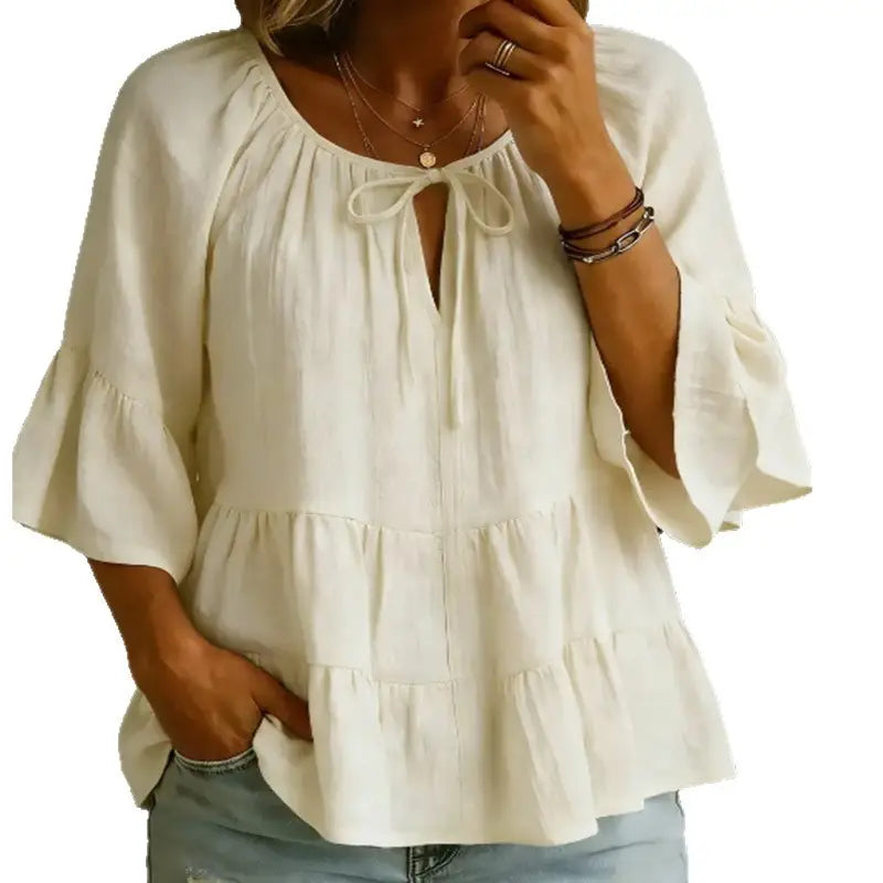Blusa de algodón y lino plisada color blanco roto, suave, con escote con lazo al frente y mangas tres cuartos acampanadas.