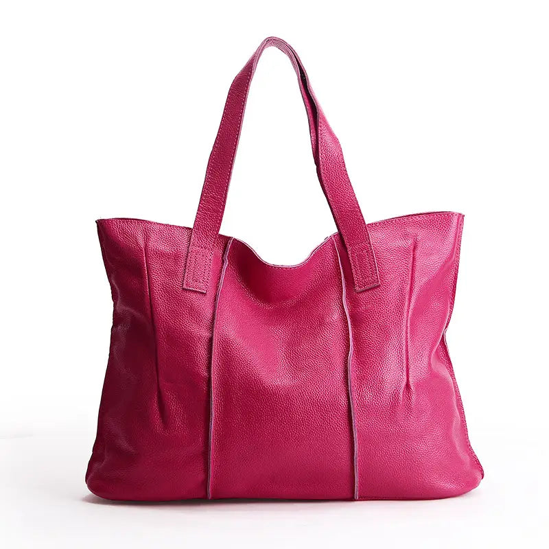 A vibrant fuchsia leather tote bag made of pebbled cowhide with a textured surface and two sturdy handles designed as a shoulder handbag.