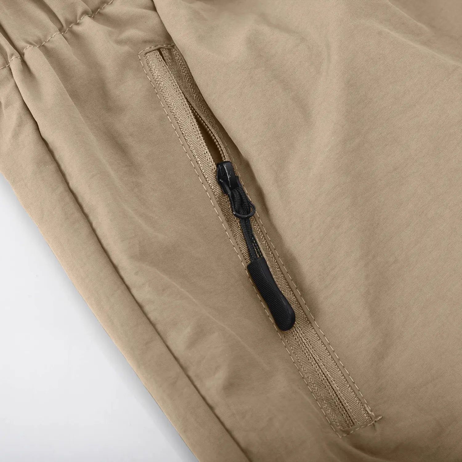 Short cargo athlétique pour hommes à jambe droite couleur beige, réalisé dans un tissu, avec une poche latérale zippée, une fermeture éclair noire et une languette de traction.