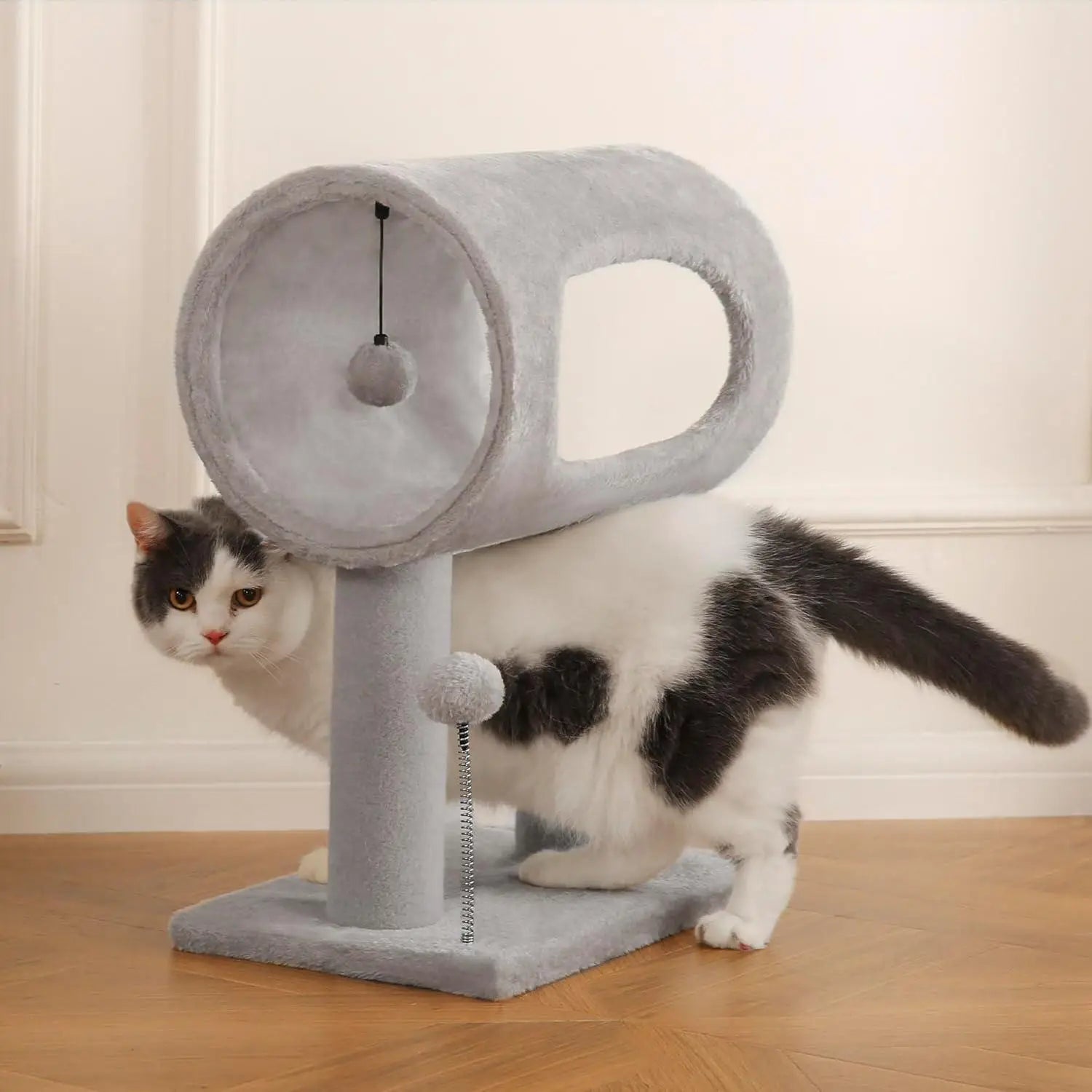 Gray plush cat tree with circular top platform and dangling ball toy featuring a tunnel and scratching post for feline entertainment and exercise.