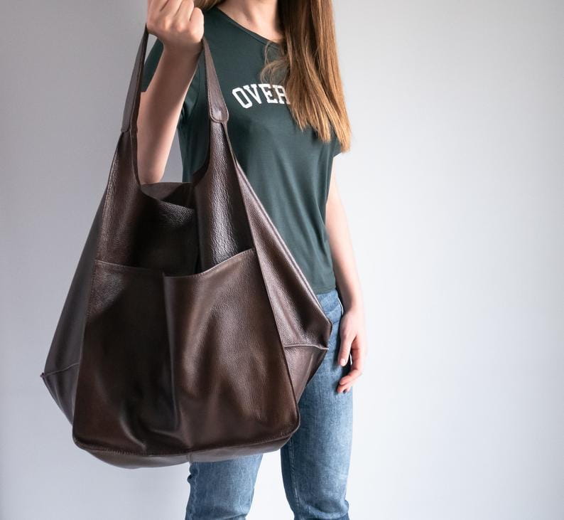 Brown leather tote bag with large capacity and soft slouchy design featuring visible stitching details.