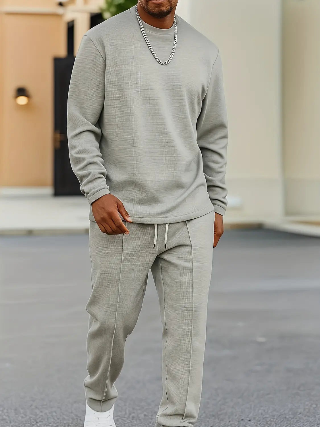 A man wearing a mens minimalist solid color sweatshirt jogger set in light gray featuring a long-sleeved sweatshirt and matching joggers with white drawstrings.