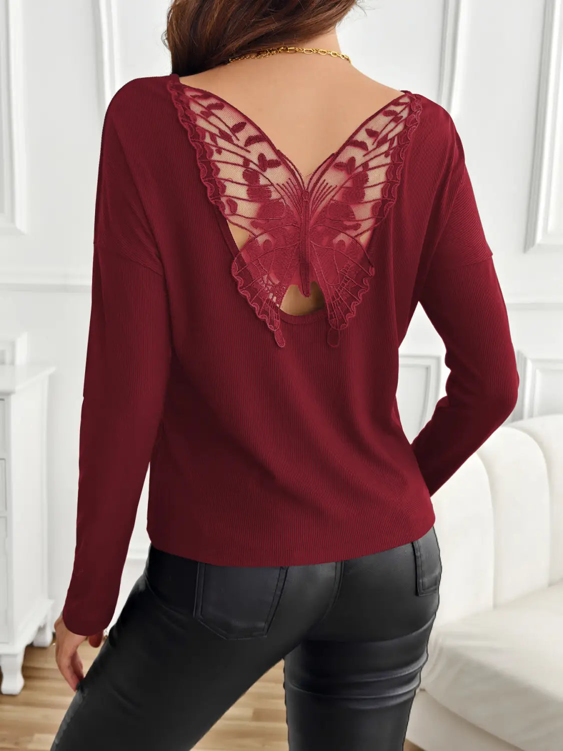 A maroon long-sleeved ribbed knit top shown from the back featuring a detailed butterfly-shaped lace design.