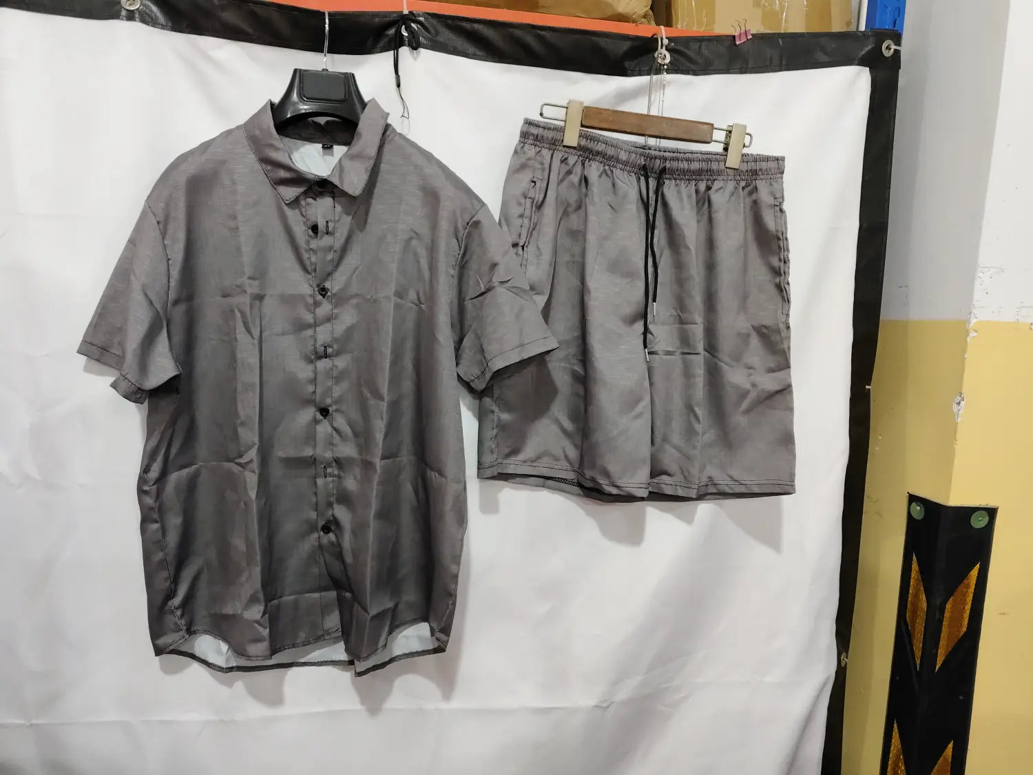 chemise en lin grise boutonnée ample et décontractée à manches courtes, avec col et poches avant, suspendue sur un cintre noir.