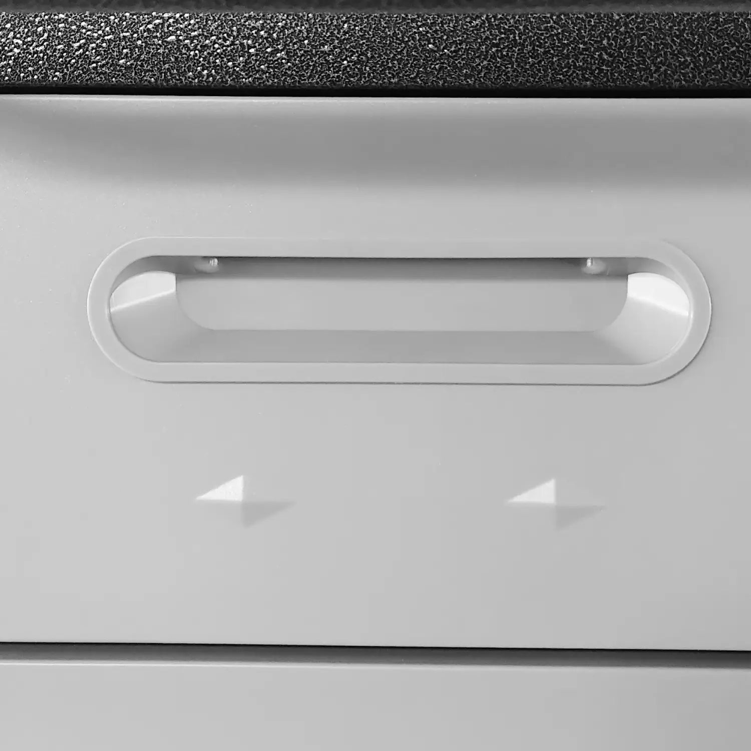 White plastic drawer handle with a sleek oval-shaped design and subtle glossy finish on a gray metal tool storage cabinet with wheels and four drawers.