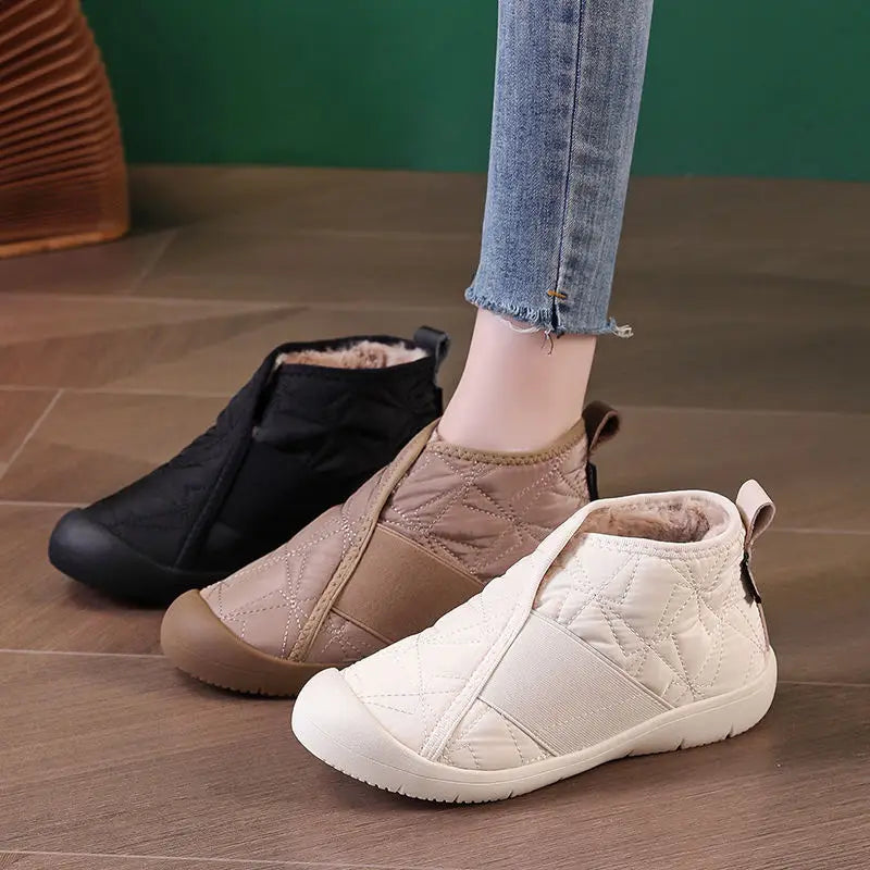 Cream-colored waterproof plush winter snow ankle boot with quilted design, brown rubber sole, and elastic side panel.