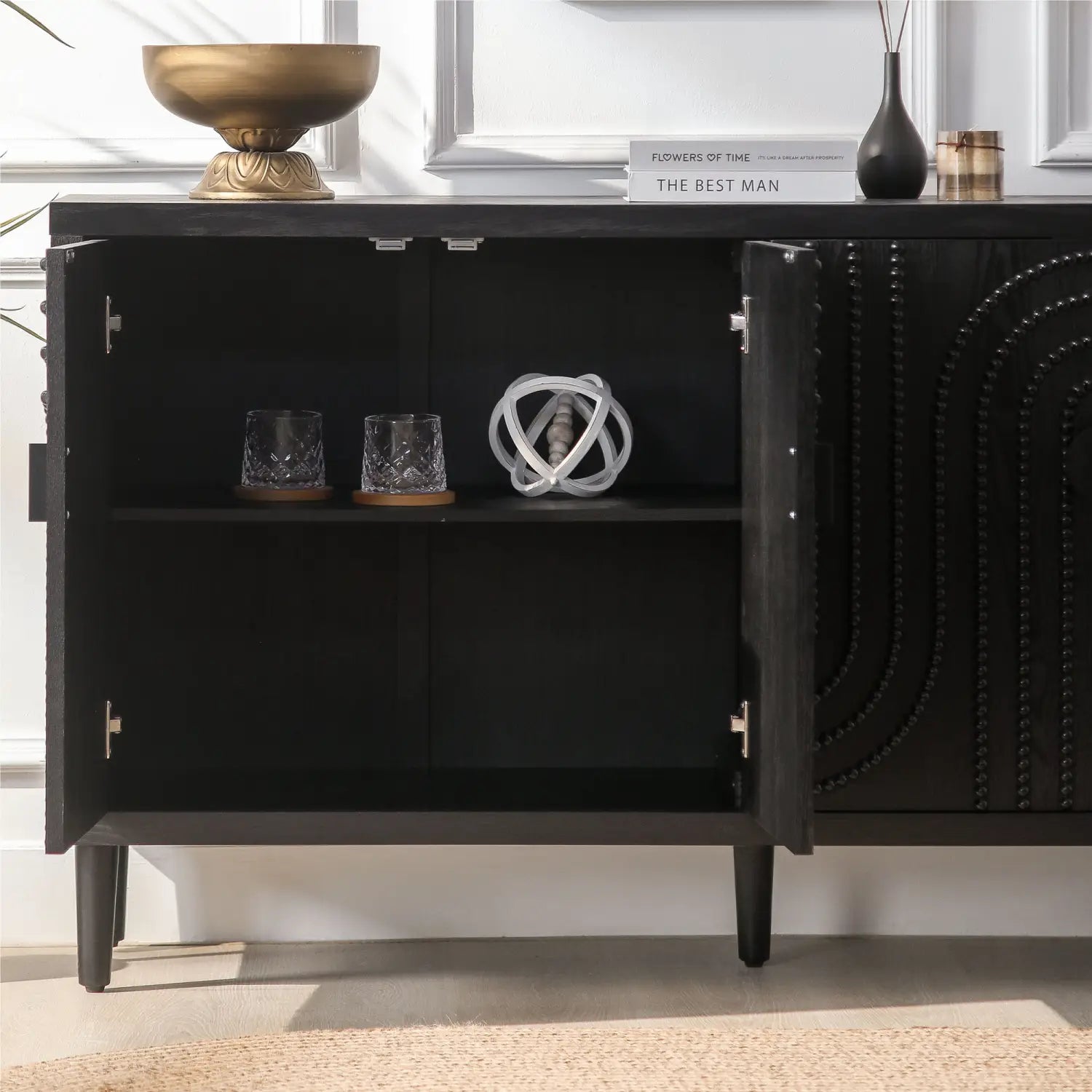 Schwarzes Sideboard-Schrankmöbel mit gebogenen Nagelkopfreißern als Akzent, mit einer bogenförmigen, perbesetzten Gestaltung und offenen Türen, die Glaswaren auf Holzuntersetzern erkennen lassen.