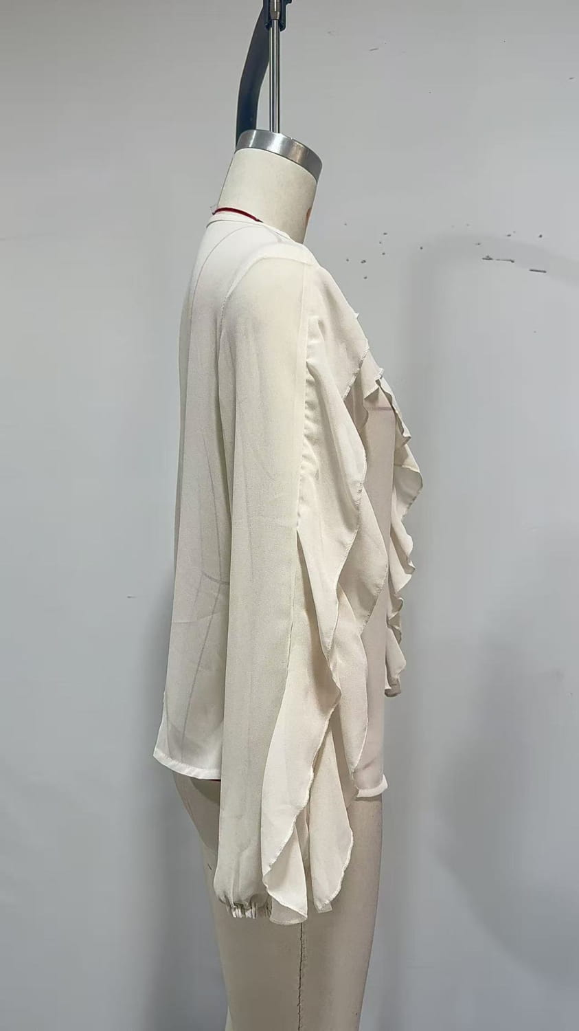Eine fließende wollweiße Chiffonbluse mit mehrlagigen Rüschen entlang der Ärmel und des Saums, auf einem Schaufensterfigürchen präsentiert für den lässigen Alltag.