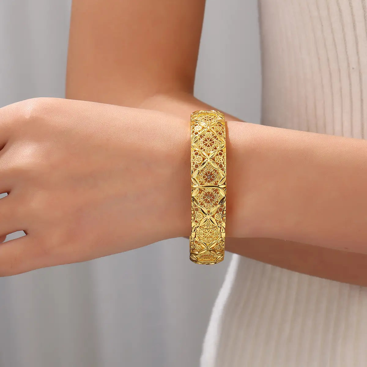 A vintage 18k gold plated four leaf clover bangle bracelet featuring a golden intricately patterned filigree design.
